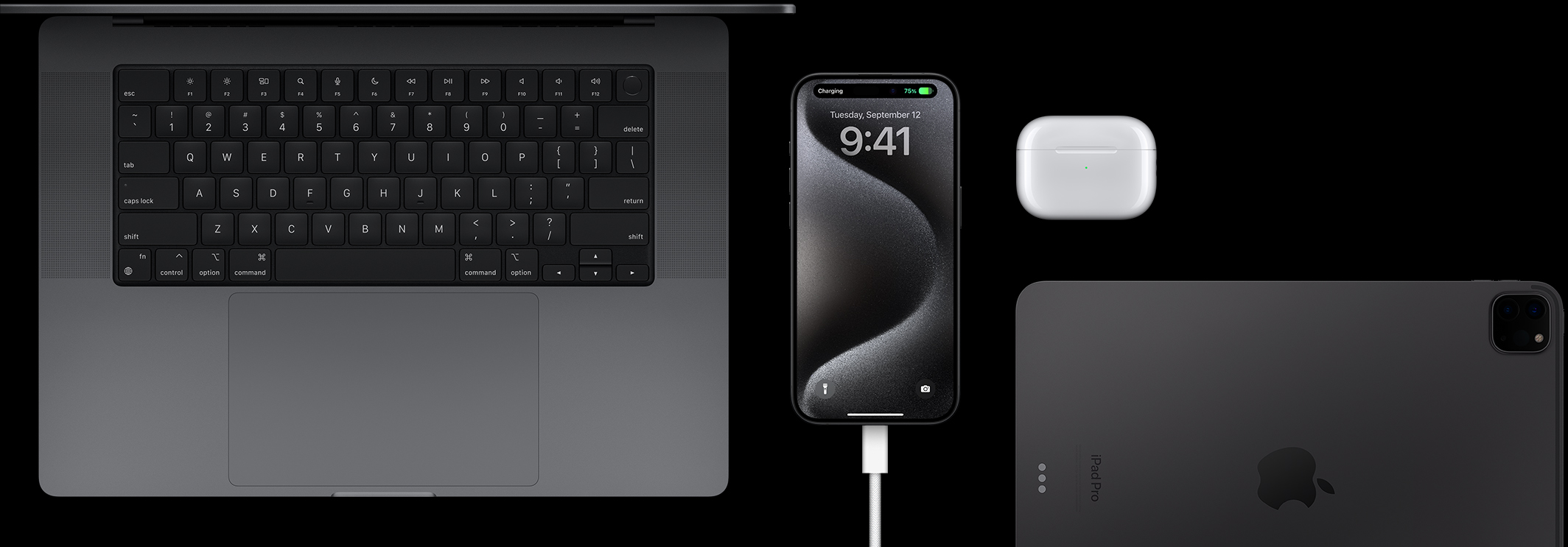 iPhone 15 Pro s připojeným USB-C kabelem, vedle kterého je Macbook Pro, AirPody Pro a iPad
