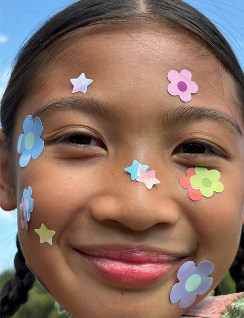 Ultranærbilde av en jente med blomsterklistremerker på ansiktet, tatt med kontinuerlig zoom på iPhone 15